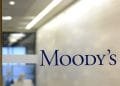 Una porta a vetri con la parola "Moody's" scritta in caratteri blu. Dietro il vetro, c'è un corridoio di un ufficio con un'illuminazione intensa e una vista sfocata di uno spazio ufficio, probabilmente dove si svolgono le discussioni sulla valutazione del Portogallo.