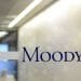 Una porta a vetri con la parola "Moody's" scritta in caratteri blu. Dietro il vetro, c'è un corridoio di un ufficio con un'illuminazione intensa e una vista sfocata di uno spazio ufficio, probabilmente dove si svolgono le discussioni sulla valutazione del Portogallo.