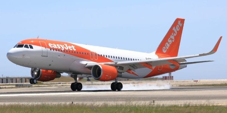 Un aereo EasyJet, dipinto nei colori bianco e arancione caratteristici della compagnia aerea, sta decollando o atterrando su una pista con una leggera scia di fumo visibile dai pneumatici. Il cielo limpido e le strutture aeroportuali sullo sfondo suggeriscono un'altra giornata impegnativa per i voli EasyJet in Portogallo.