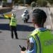 Un agente di polizia con berretto verde e gilet giallo con la scritta "GNR" dirige il traffico su una strada, rispettando la legge moto portogallo. Un altro agente con un gilet giallo segnala ai veicoli in arrivo, mentre due agenti in motocicletta vengono fermati nelle vicinanze. I pedoni stanno sul marciapiede osservando la scena.