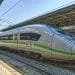 Un elegante treno ad alta velocità ICE (InterCity Express) color argento con una striscia verde è parcheggiato su un binario della stazione ferroviaria sotto una struttura coperta, che ricorda la realizzazione TGV portogallo. La scena è ben illuminata con il cielo sereno sullo sfondo.