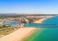 Veduta aerea di una città costiera dell'Algarve, portogallo, caratterizzata da un grande porto turistico con numerose barche ormeggiate, spiagge sabbiose che si estendono lungo la costa e un mix di edifici sparsi in tutta la città. L'oceano è di un turchese vibrante e il cielo è limpido, ideale per avventure in multiproprietà.