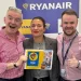 Annunciando nuovi voli Ryanair verso il Portogallo, Michael O'Leary solleva con entusiasmo un cartello blu con la scritta "ROMA 2024", "7 NUOVE ROTTE" e "RYANAIR".