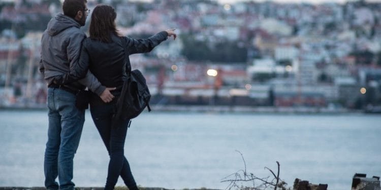 Una coppia si trova sul lungomare, con l'uomo che abbraccia la donna da dietro. La donna, in giacca nera, indica gli edifici dall'altra parte dell'acqua, forse sognando quando i giovani potrebbero comprare casa in Portogallo. L'area attorno a loro presenta alcuni detriti e ramoscelli. Lo sfondo è un paesaggio urbano con vari edifici.