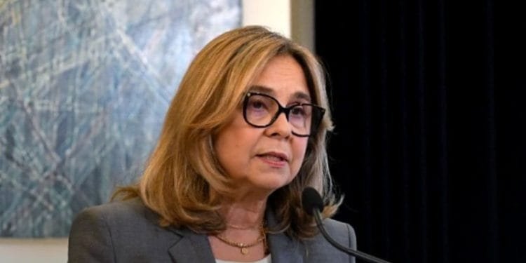 Una donna dai capelli biondi, con gli occhiali e un blazer grigio, parla al microfono. Ha un'espressione seria e sta di fronte a un dipinto astratto geometrico, discutendo del ruolo di un medico famiglia in Portogallo.