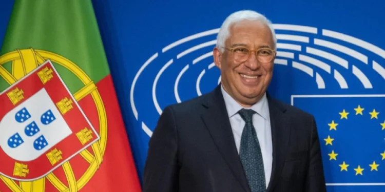 Antonio Costa, eletto Presidente del Consiglio Europeo sorride davanti a due bandiere: quella portoghese a sinistra e quella dell'Unione Europea a destra. Lo sfondo è un muro blu con linee circolari bianche. È un uomo in giacca e cravatta
