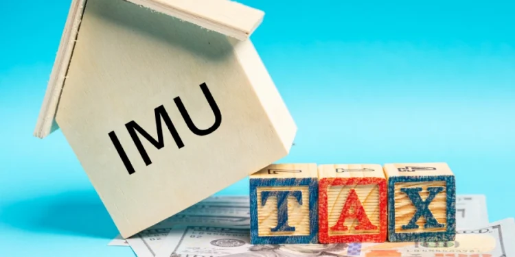 Su una pila di banconote da un dollaro si erge una casetta di legno con la scritta Esenzione IMU su un lato e fa riferimento all'estero aire. Davanti alla casa, tre blocchi colorati compongono la scritta "TAX" su uno sfondo blu.