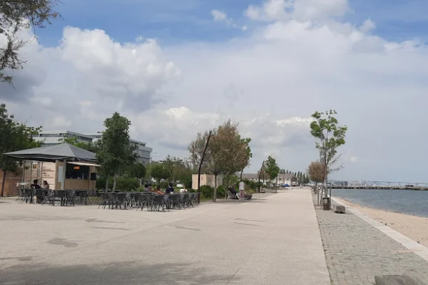 Sul Tejo a Lisbona un chiosco con posti a sedere e il cui nome è Lamiré con una tettoia di metallo grigio. Alcuni si godono i posti a sedere ai tavoli, altri invece passeggiano. Il cielo è parzialmente nuvoloso con macchie di blu e il fiume calmo è sul lato destro dell'immagine.