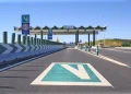 Vista di un casello con luci verdi e occasionalmente luce gialla su un'autostrada portoghese con segnaletica di Via Verde. Un segnale di limite di velocità di 60 km/h è visibile accanto ai caselli automatizzati. La strada è libera con frecce direzionali e spartitraffico che guidano i veicoli.