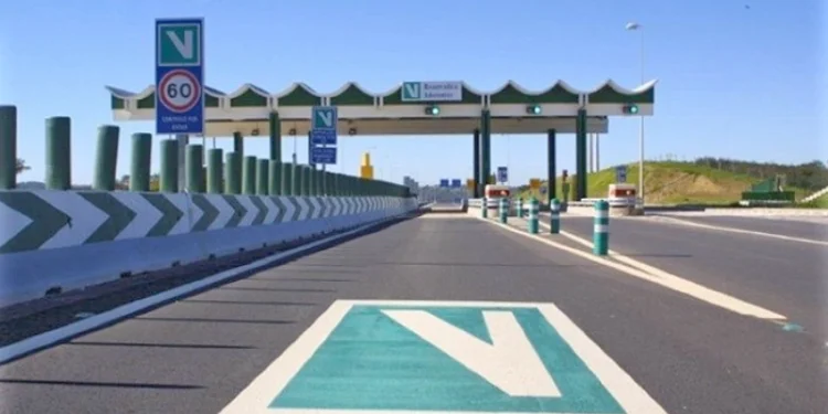 Vista di un casello con luci verdi e occasionalmente luce gialla su un'autostrada portoghese con segnaletica di Via Verde. Un segnale di limite di velocità di 60 km/h è visibile accanto ai caselli automatizzati. La strada è libera con frecce direzionali e spartitraffico che guidano i veicoli.