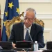 Il presidente della repubblica portoghese è seduto a una scrivania decorata e firma il piano per una riduzione IRS. Dietro di lui ci sono le bandiere del Portogallo e dell'Unione Europea. Marcelo rebelo de Sousa appare concentrato sul suo lavoro, con microfoni e una bottiglia d'acqua sulla scrivania davanti a lui.