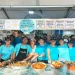 Un gruppo di persone dello staff della "Festa da Ria Formosa" sta dietro un bancone delle sagre del pesce in Algarve, Portogallo. Stanno sorridendo e posando con vari piatti di pesce sul bancone di fronte a loro, tra cui paella, crostacei e aragosta. I menu del cibo sono visualizzati sopra di loro.
