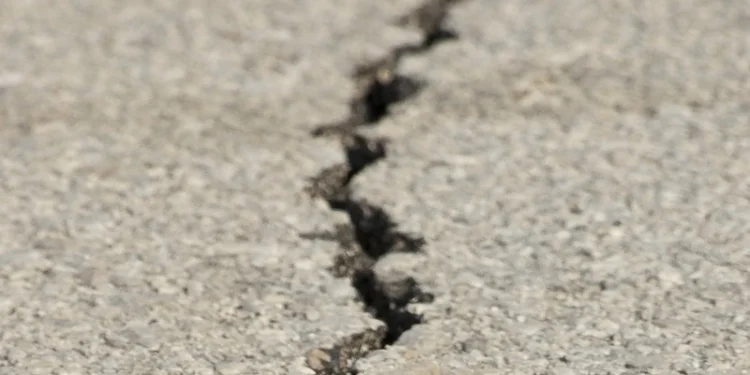 Immagine ravvicinata di una crepa su una superficie di cemento simile alle conseguenze di un epicentro di terremoto in Portogallo. La crepa si estende in diagonale attraverso l'immagine, con larghezze variabili e bordi frastagliati, indicando possibili danni. Il cemento circostante appare ruvido e strutturato.