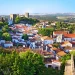 Una vista panoramica della cose da vedere nella città storica a Obidos con edifici bianchi e tetti di tegole rosse racchiusi da antiche mura in pietra. La città è circondata da rigogliosi alberi verdi e dolci colline sotto un cielo azzurro e terso.