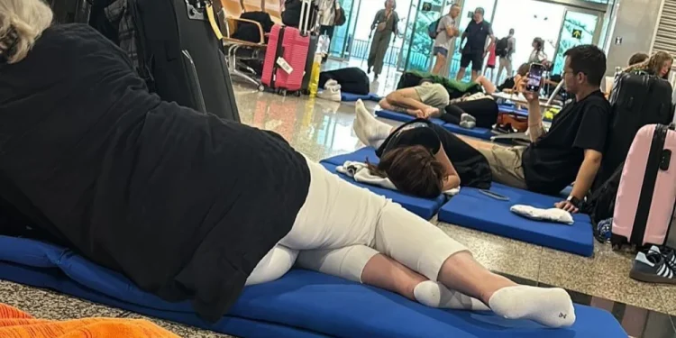 Immagini della disavventura dei turisti italiani bloccati all'aeroporto di Madeira mentre riposano su tappetini blu sul pavimento. A causa di ritardi o cancellazioni. I bagagli sono sparsi in giro e alcune persone sono sedute o camminano sullo sfondo vicino ai gate e alle aree salotto.