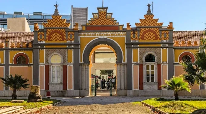 La Biblioteca Municipale di Faro dove Enrico Berardi presenta il libro Jugaad. Nella foto vi è un edificio storico colorato con una facciata ornata e simmetrica con motivi a zigzag gialli e marroni si erge fiero sotto un cielo azzurro terso. Le grandi finestre ad arco e l'ingresso centrale ne accrescono il fascino.