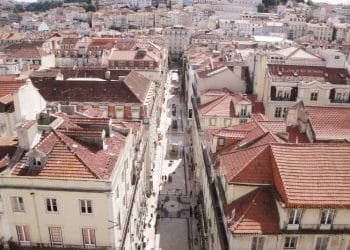 Una vista aerea di Lisbona con strade strette e palazzi fitti e dai tetti rossi, stando all'andamento degli affitti in Portogallo. Le strade sono piene di pedoni e fiancheggiate da edifici a più piani, dando un senso di densità urbana e uniformità architettonica.