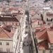 Una vista aerea di Lisbona con strade strette e palazzi fitti e dai tetti rossi, stando all'andamento degli affitti in Portogallo. Le strade sono piene di pedoni e fiancheggiate da edifici a più piani, dando un senso di densità urbana e uniformità architettonica.