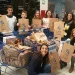 Un gruppo di sette volontari, sorridenti e con in mano borse per la raccolta del Banco Alimentar in Portogallo. Posano insieme in un centro commerciale e hanno riempito due carrelli della spesa con borse per una raccolta alimentare. Un piccolo albero di Natale è visibile sullo sfondo, aggiungendo un tocco festoso.