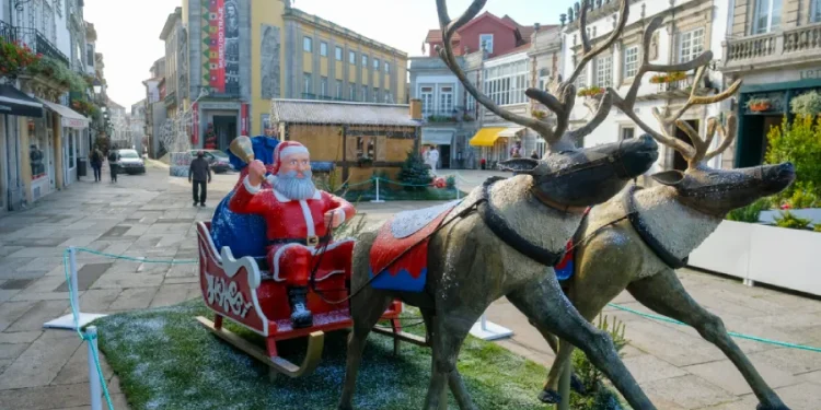Una scena festosa nelle affascinanti strade di Viana do Castelo mostra Babbo Natale che cavalca una slitta trainata da renne. L'architettura storica è spolverata di neve artificiale, mentre negozi e alcuni pedoni completano questa incantevole cornice di eventi natalizie.
