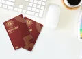 Due esemplari del Nuovo Passaporto elettronico portoghese sono su una scrivania bianca de designer accanto a una tastiera, un mouse per computer, una tazza di caffè fumante e campioni di colori vivaci. La scena cattura l'essenza del flusso creativo, forse come parte di un design da concorso stimolante.