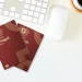 Due esemplari del Nuovo Passaporto elettronico portoghese sono su una scrivania bianca de designer accanto a una tastiera, un mouse per computer, una tazza di caffè fumante e campioni di colori vivaci. La scena cattura l'essenza del flusso creativo, forse come parte di un design da concorso stimolante.