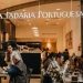 Le persone siedono ai tavoli della famosa catena di caffè A Padaria Portuguesa immerse in conversazioni o usando computer portatili. Una donna serve con grazia i clienti, esaltando l'atmosfera calda e invitante con il suo arredamento moderno.