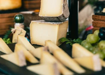 Un'esposizione di formaggi gourmet a marchio Pingo Doce su un vassoio, con spicchi grandi e piccoli di delizie semidure, circondati da uva verde e felci. Questa disposizione rustica evoca l'eleganza di Il Trionfo dei Formaggi, richiamando le visioni delle degustazioni dei World Cheese Awards 2024.