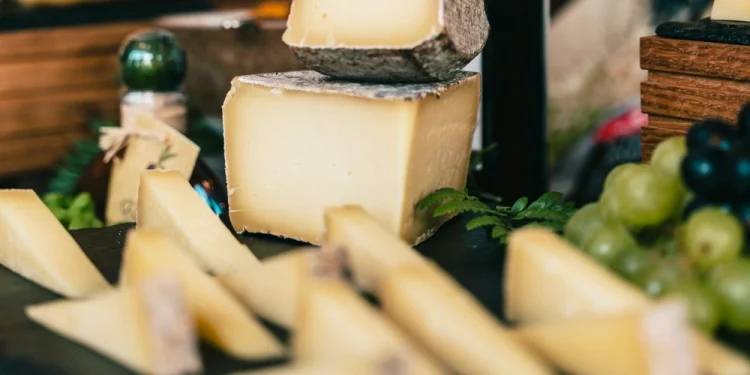 Un'esposizione di formaggi gourmet a marchio Pingo Doce su un vassoio, con spicchi grandi e piccoli di delizie semidure, circondati da uva verde e felci. Questa disposizione rustica evoca l'eleganza di Il Trionfo dei Formaggi, richiamando le visioni delle degustazioni dei World Cheese Awards 2024.