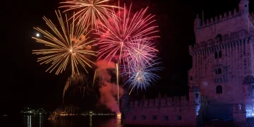 Con un meteo favorevole, nel cielo i fuochi d'artificio colorati scoppiano sulla torre di Belem vicino al fiume Tejo nella notte di Capodanno a Lisbona in Portogallo. Il cielo è illuminato da rossi, arancioni e blu brillanti, che si riflettono nell'acqua calma sottostante, creando una scena abbagliante.