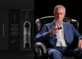 José Mourinho in abito blu siede su una sedia di pelle nera, assaporando un bicchiere di vino rosso. A sinistra, una scatola di vino aperta con l'etichetta "The Special One", con l'immagine di una bottiglia di vino all'interno. Lo sfondo è nero, il che esalta la raffinatezza della scena.