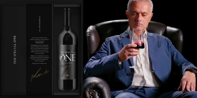 José Mourinho in abito blu siede su una sedia di pelle nera, assaporando un bicchiere di vino rosso. A sinistra, una scatola di vino aperta con l'etichetta "The Special One", con l'immagine di una bottiglia di vino all'interno. Lo sfondo è nero, il che esalta la raffinatezza della scena.