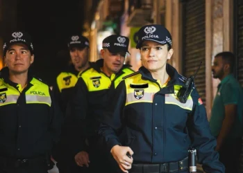 Un gruppo di cinque poliziotti in uniforme pattuglia una strada scarsamente illuminata, incarnando la promessa di Lisbona città sicura. Indossano berretti e portano radio, con una donna a capo dell'attenta squadra. Lo sfondo mostra una vetrina chiusa, evidenziando la loro presenza vigile.