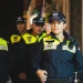 Un gruppo di cinque poliziotti in uniforme pattuglia una strada scarsamente illuminata, incarnando la promessa di Lisbona città sicura. Indossano berretti e portano radio, con una donna a capo dell'attenta squadra. Lo sfondo mostra una vetrina chiusa, evidenziando la loro presenza vigile.