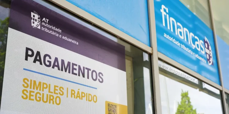 Cartelli su una vetrata di un ufficio della Financas portoghese annunciano le Nuove Norme Fiscali. Un cartello promuove pagamenti facili e sicuri con un codice QR, l'autorità fiscale. Gli alberi si riflettono dolcemente nel vetro.