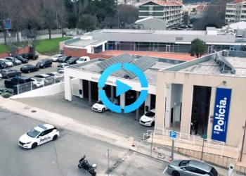 Vista aerea della stazione di polizia a Porto con diverse auto della polizia parcheggiate all'esterno in servizio contro il parcheggio irregolare. L'edificio mostra un grande cartello "Polícia" e presenta pannelli solari sul tetto. Circondata da edifici residenziali sullo sfondo.