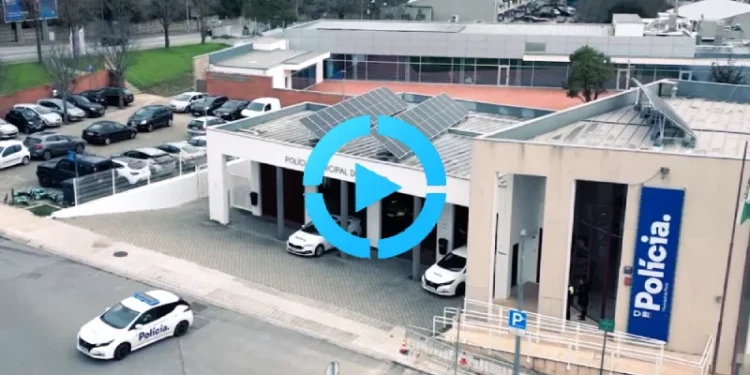 Vista aerea della stazione di polizia a Porto con diverse auto della polizia parcheggiate all'esterno in servizio contro il parcheggio irregolare. L'edificio mostra un grande cartello "Polícia" e presenta pannelli solari sul tetto. Circondata da edifici residenziali sullo sfondo.