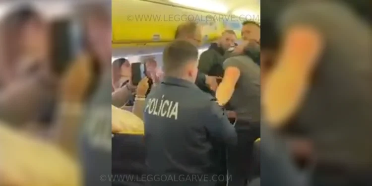 Agenti di polizia all'interno del corridoio di un aereo Ryanair, intenti a gestire una situazione che coinvolge un passeggero molesto. Alcuni passeggeri sono seduti e osservano l'evento.