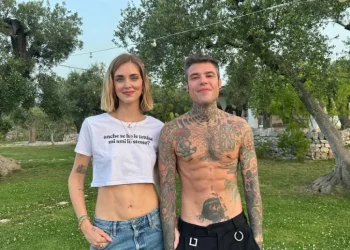 Chiara Ferragni con un crop top bianco e jeans è in piedi accanto a Fedez senza maglietta con tatuaggi in un'area erbosa con alberi, non in Portogallo, bensì sono in Puglia. Sorridono sotto le luci scintillanti, catturando l'essenza di un'atmosfera.
