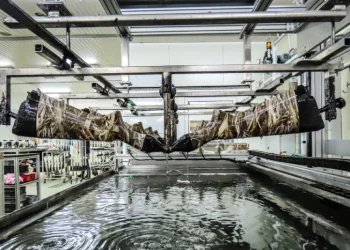L'interno della fabbrica armi di Viana Castelo, un fucile viene immerso in una vasca d'acqua per un processo di stampa idrografica presso la Browning Viana. L'imbracciatura dei fucili con motivo mimetico risaltano mentre altri attendono il loro turno sullo sfondo.