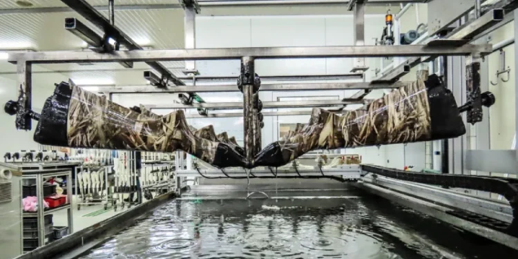 L'interno della fabbrica armi di Viana Castelo, un fucile viene immerso in una vasca d'acqua per un processo di stampa idrografica presso la Browning Viana. L'imbracciatura dei fucili con motivo mimetico risaltano mentre altri attendono il loro turno sullo sfondo.