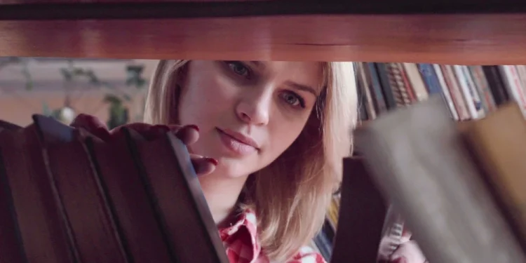 Una ragazza di un gruppo lettura, con i capelli biondi e una camicia a quadri rossa, sta cercando attentamente tra i libri su uno scaffale a Lisbona.