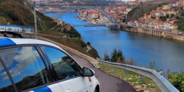 Un'auto della polizia è parcheggiata su una strada che si affaccia sulla città di Porto, come descritto nel Rapporto Sicurezza Interna 2024. Il ponte attraversa la città con edifici colorati sulla collina. Sulla fiancata dell'auto c'è scritto "Polícia" e il cielo è parzialmente nuvoloso.