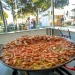 Tra gli eventi c'è una grande padella di paella di pesce che mostra gamberi e cozze in esposizioni in un festival all'aperto in Algarve. Sullo sfondo, ci sono tavoli, alberi e tende, che suggeriscono un'atmosfera festosa piena dei sapori vibranti.
