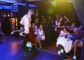 All'interno del ristorante Magic Moment, uno spettacolo di un artista sul palco crea intrattenimento togliendosi la camicia davanti a un pubblico coinvolto. L'atmosfera ricorda quella di un raffinato spettacolo sexy, con tavoli ornati da bicchieri di vino e clienti completamente divertiti dallo show.