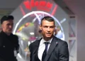 Cristiano Ronaldo in abiti eleganti all'ingresso di un cinema. Si vede sfuocato sullo sfondo un altro uomo con un cappellino e un'insegna luminosa.