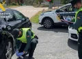 Due agenti della Guardia Civil con giubbotti ad alta visibilità ispezionano un'auto nera a un posto di blocco stradale durante un'operazione di controllo del gasolio in Spagna. Un agente esamina il carburante mentre l'altro prende appunti, con le auto della polizia parcheggiate nelle vicinanze.