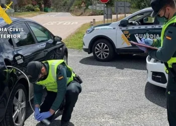 Due agenti della Guardia Civil con giubbotti ad alta visibilità ispezionano un'auto nera a un posto di blocco stradale durante un'operazione di controllo del gasolio in Spagna. Un agente esamina il carburante mentre l'altro prende appunti, con le auto della polizia parcheggiate nelle vicinanze.