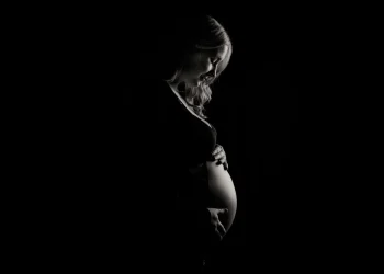 Un'immagine in bianco e nero ritrae una donna incinta di profilo, che si culla delicatamente il pancione con entrambe le mani, simbolo in Portogallo della legge contro la violenza ostetrica. La luce soffusa ne esalta l'espressione serena.