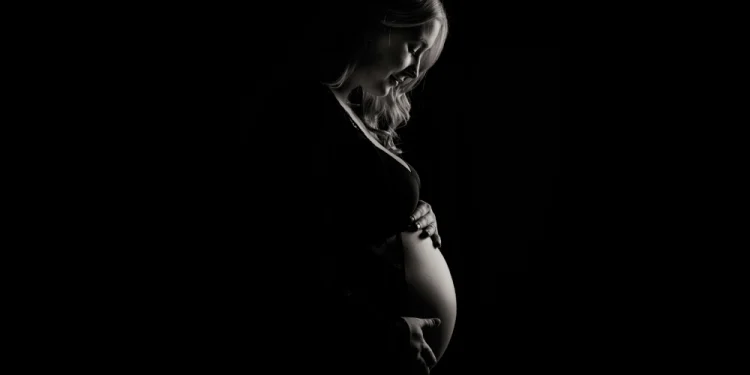 Un'immagine in bianco e nero ritrae una donna incinta di profilo, che si culla delicatamente il pancione con entrambe le mani, simbolo in Portogallo della legge contro la violenza ostetrica. La luce soffusa ne esalta l'espressione serena.